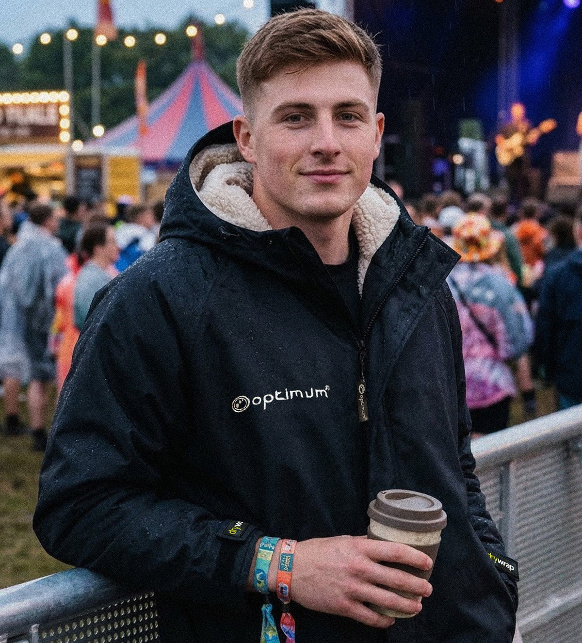 Lifestyle photo of man in black Optimum fleece-lined changing robe holding coffee at an outdoor festival - Optimum