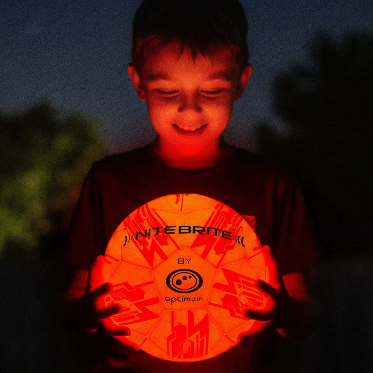 Boy holding a glowing orange Nite Brite by Optimum football in the dark - Optimum